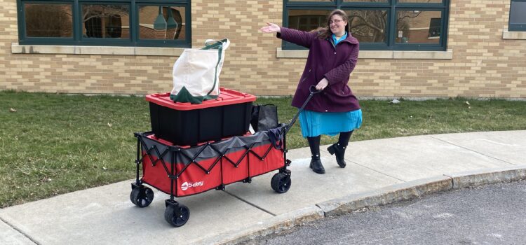 Library staff posing with large collapsible wagon filled with tote bags and bins visiting Hornell's Elderwood.